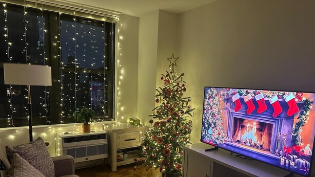 Un saló acollidor amb un televisor que mostra una escena nadalenca, un arbre de Nadal i una finestra amb llums enfilades.