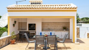 Eine Terrasse im Freien mit Esstisch, Stühlen und Grillplatz.