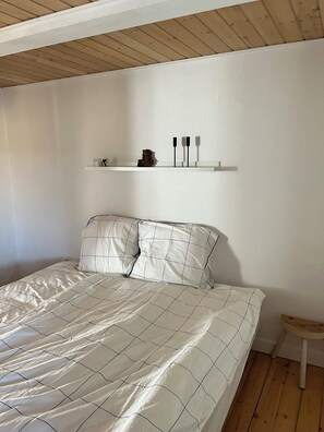 A bedroom with a bed, a small stool, a shelf with decorative items, and a wooden ceiling. - Charming house with beautiful views (Gedser)