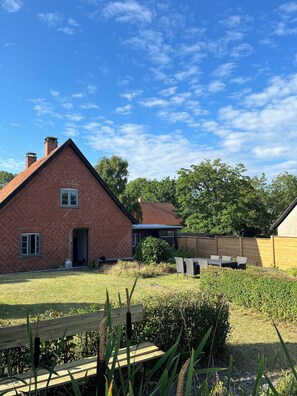 A brick house with a sloped roof, a small attached structure, and a fenced yard with a bench and table. - Charming house with beautiful views (Gedser)