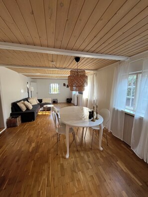 A spacious living area with a wooden ceiling, a round dining table, and a black sofa. - Charming house with beautiful views (Gedser)