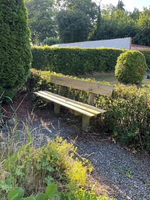 A wooden bench in a garden with gravel ground, surrounded by greenery and a hedge. - Charming house with beautiful views (Gedser)
