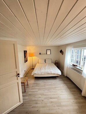 A bedroom with a bed, a chair, a lamp, a window, and a door. - Charming house with beautiful views (Gedser)