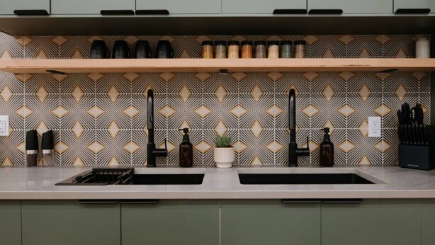 A kitchen with two sinks, a patterned backsplash, and a shelf above the countertop.