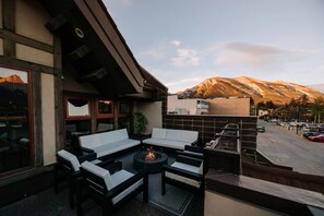 Un espace extérieur aménagé avec un foyer, des bancs blancs dotés de coussins et une vue sur une montagne.