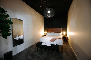 A hotel room with a large bed, bedside lamps, a mirror, and a hanging light fixture. - Sevenfold | Sleeps 20 | Luxe 7BR Retreat + Hot Tub (Canmore)
