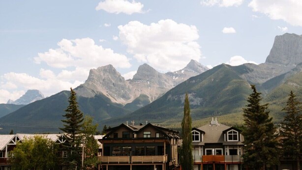 A mountain landscape with a residential area in the foreground featuring houses with balconies and a clear sky.