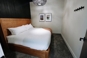 Une chambre avec un lit en bois, du linge de lit blanc, un mur foncé et deux tableaux encadrés.