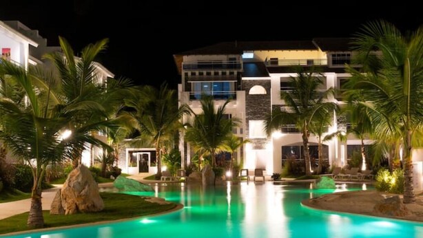 Um hotel com piscina, palmeiras e fachada bem iluminada.
