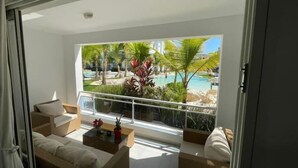Uma sala de estar moderna com uma janela grande que dá para uma piscina e um jardim tropical.