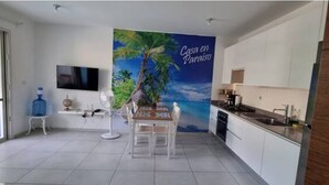 A modern kitchen with white cabinets, a dining area with a table and chairs, a large water dispenser, and a TV mounted on the wall. - El Paraiso apartment (Dominicus)