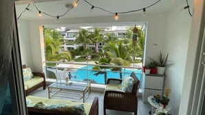 A balcony with a glass table, wicker chairs, and a view of a swimming pool and palm trees. - El Paraiso apartment (Dominicus)