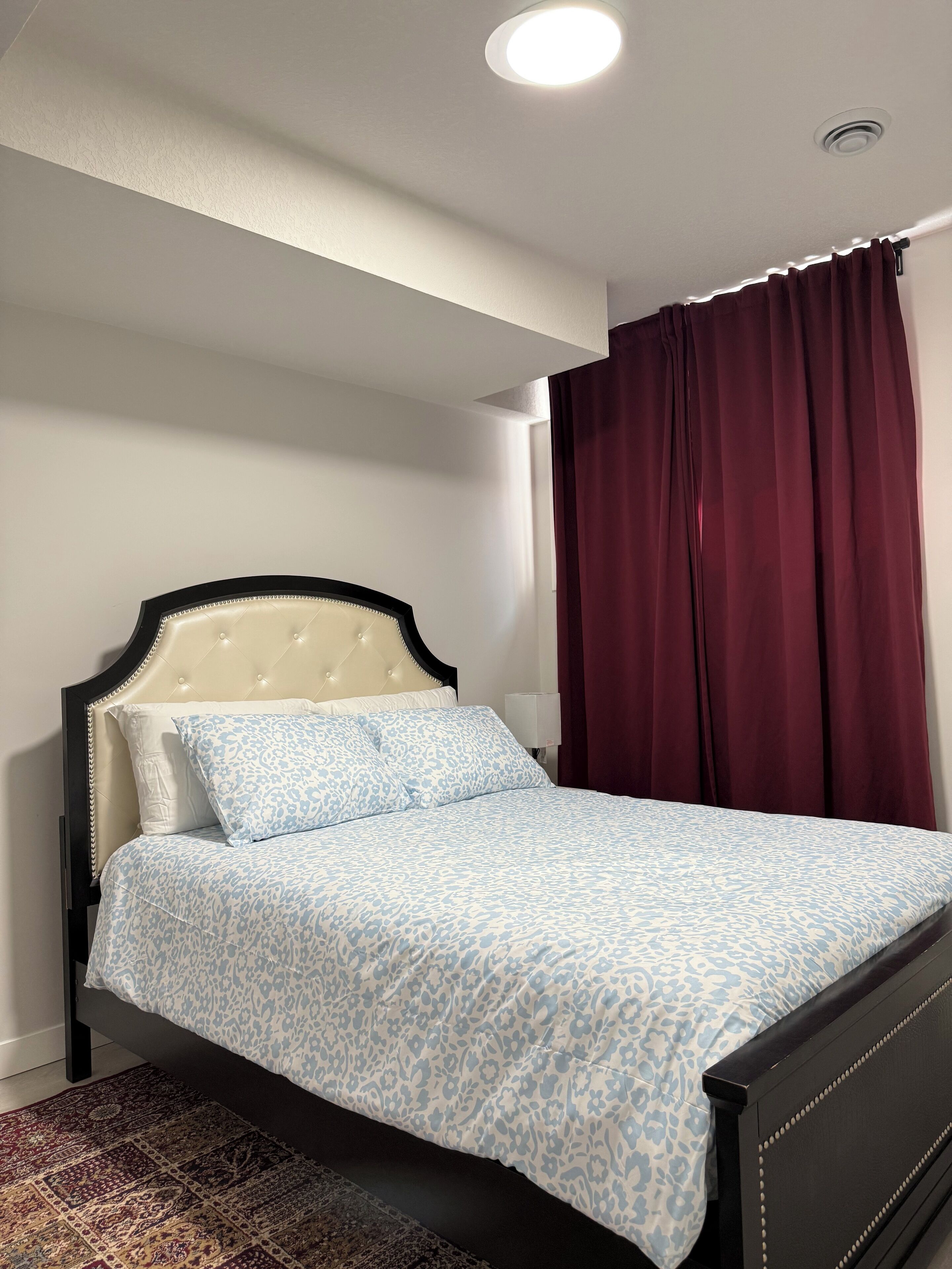 A bedroom with a bed, a nightstand, a lamp, and a window with curtains.