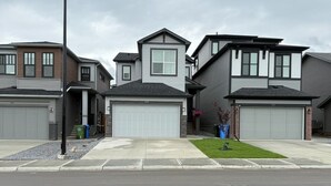 A row of modern two-story houses with attached garages, a well-maintained lawn, and a clear sky.