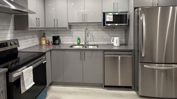 A modern kitchen with stainless steel appliances, grey cabinets, and a tiled backsplash.