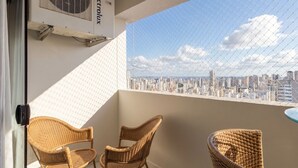 A balcony with two wicker chairs, a small table, and a city view through a chain-link fence. - BLI - Complete Condominium With gym and Pool in Goiania (Goiânia)