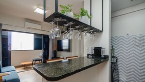 A modern kitchen with a granite countertop, hanging wine glasses, a built-in TV, and a coffee machine. - BLI - Complete Condominium With gym and Pool in Goiania (Goiânia)