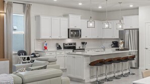 Eine moderne Küche mit weißen Schränken, Edelstahlgeräten und einer Bar mit Sitzgelegenheiten.