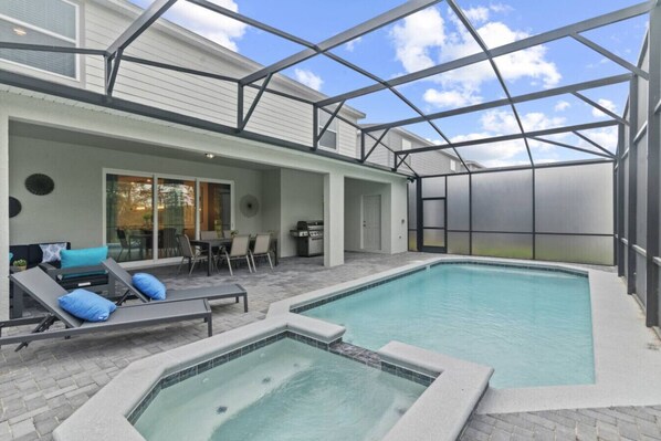 A covered outdoor swimming pool with lounge chairs and a grill area.