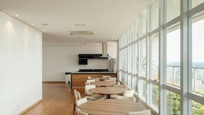 Una cocina moderna con una isla central, amplios ventanales con vista a la ciudad y una zona de comedor con mesas y sillas redondas.