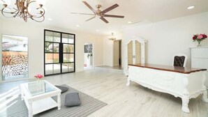 A spacious living room with a white sofa, a glass coffee table, a white fireplace, and a ceiling fan. - 10Mins to airport (San Antonio)