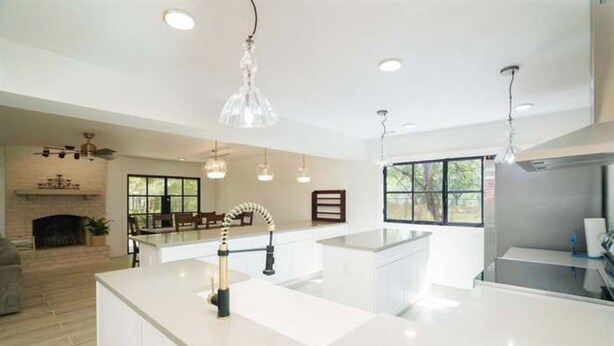 A modern kitchen with a central island, pendant lighting, and a fireplace in the background. - 10Mins to airport (San Antonio)