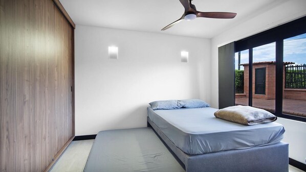 A bedroom with a bed, a ceiling fan, and a window with a view of a brick building.