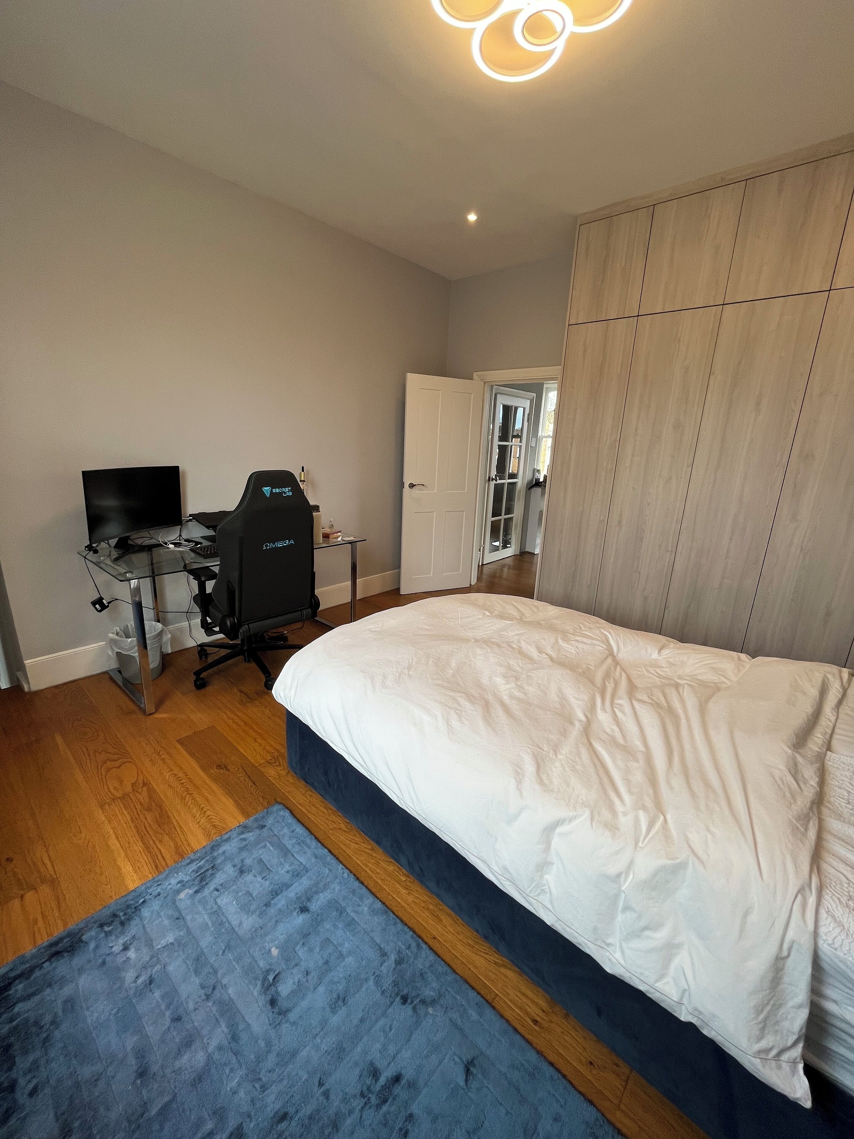 Een slaapkamer met een bed, een bureau met een computer en een kledingkast.
