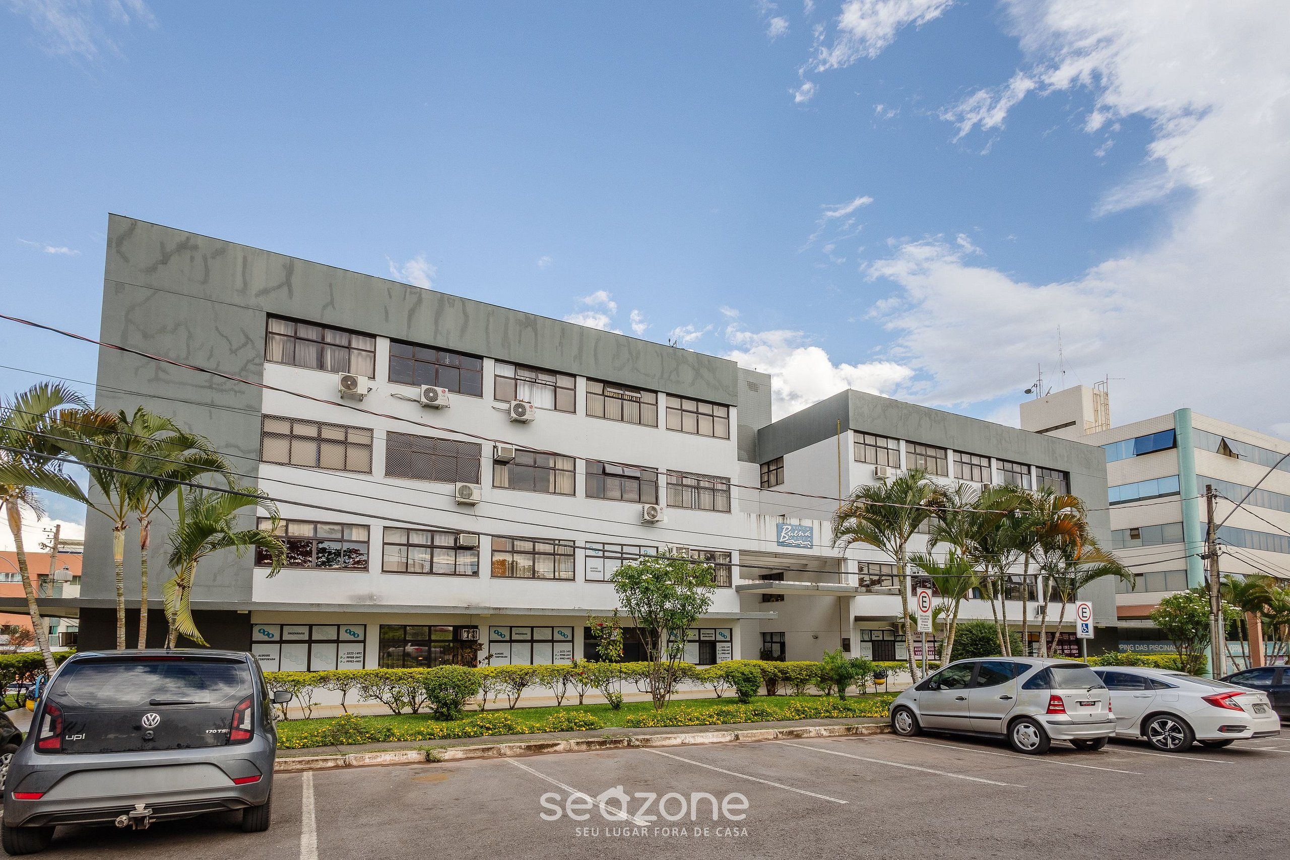 Un edificio moderno de varios pisos, con unidades de aire acondicionado y un estacionamiento con varios automóviles.