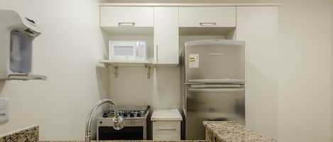 A compact kitchenette with a microwave, a stainless steel refrigerator, a gas stove, and a sink.