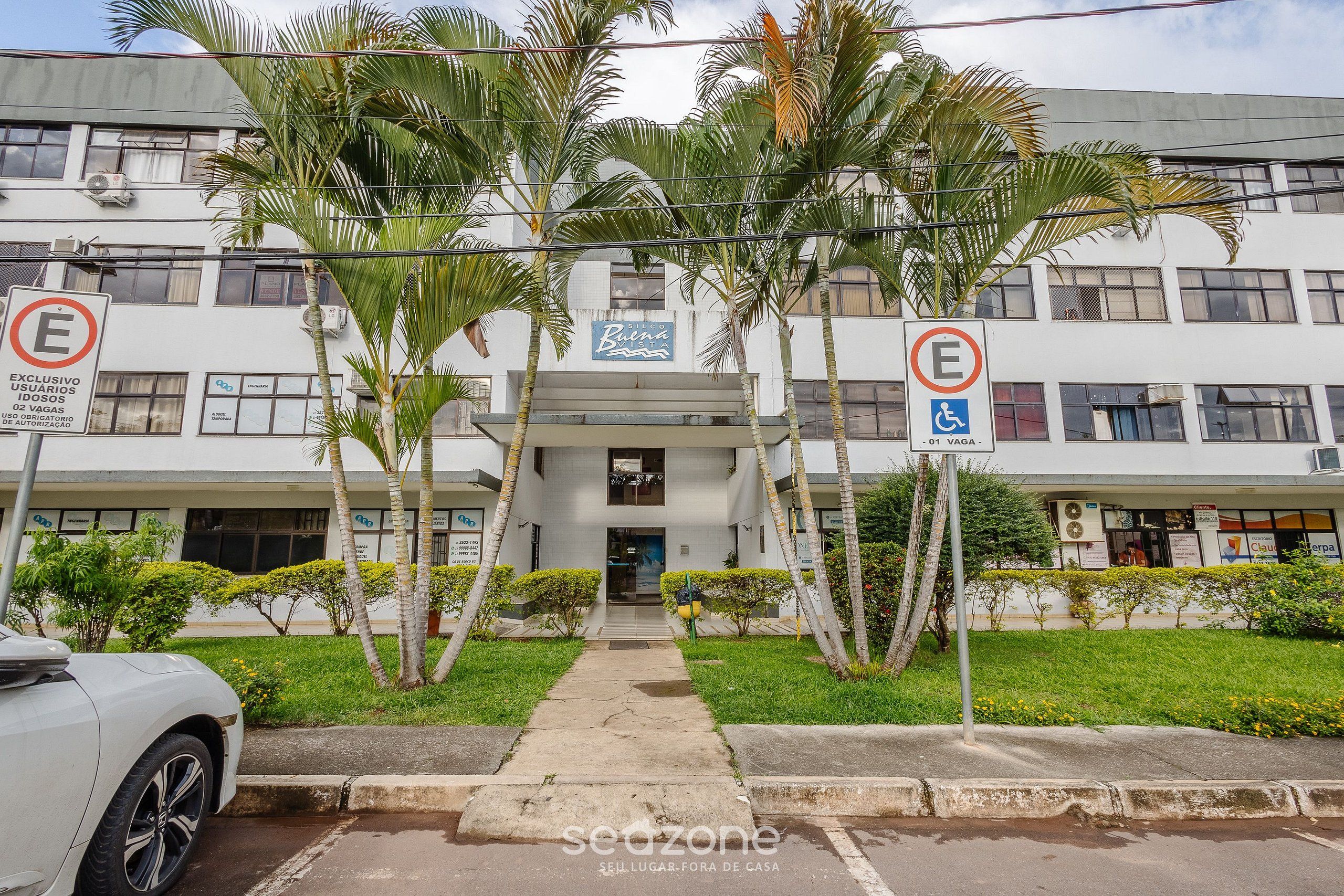 Un edificio con un letrero que indica que es un hotel. Se ven palmeras y un camino que lleva a la entrada.