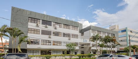 A modern building with multiple floors, air conditioning units, and a parking lot with several cars.