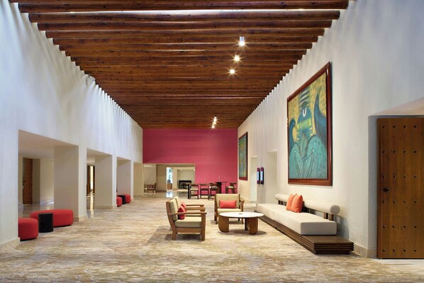 A spacious lobby with a high wooden ceiling, red walls, and a large painting. There are multiple seating areas with red and beige furniture.