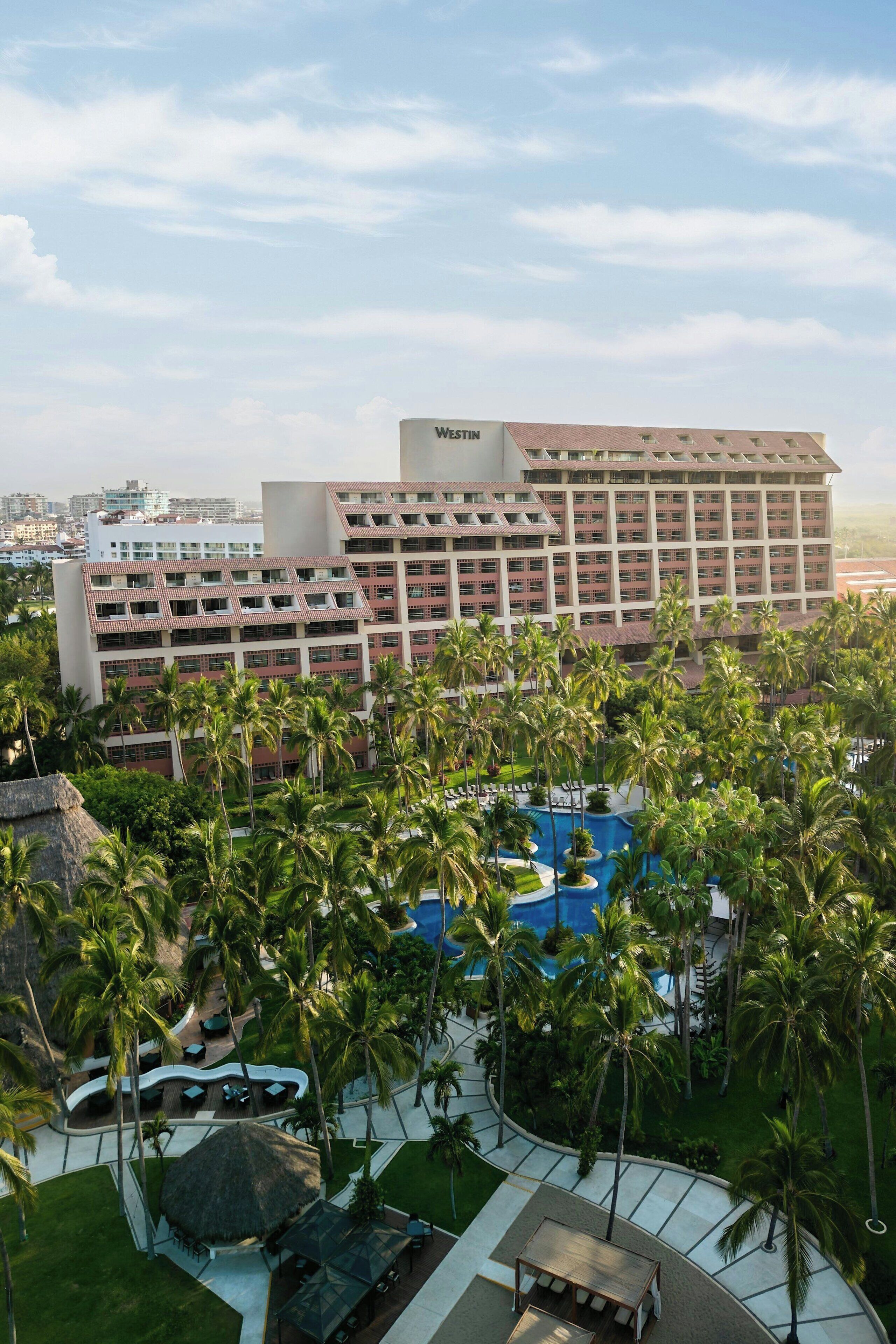 A hotel with multiple floors, a swimming pool, and palm trees.