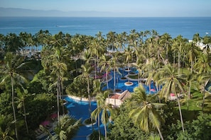 Un resort con un amplio área de piscina rodeada de palmeras y vistas al océano.