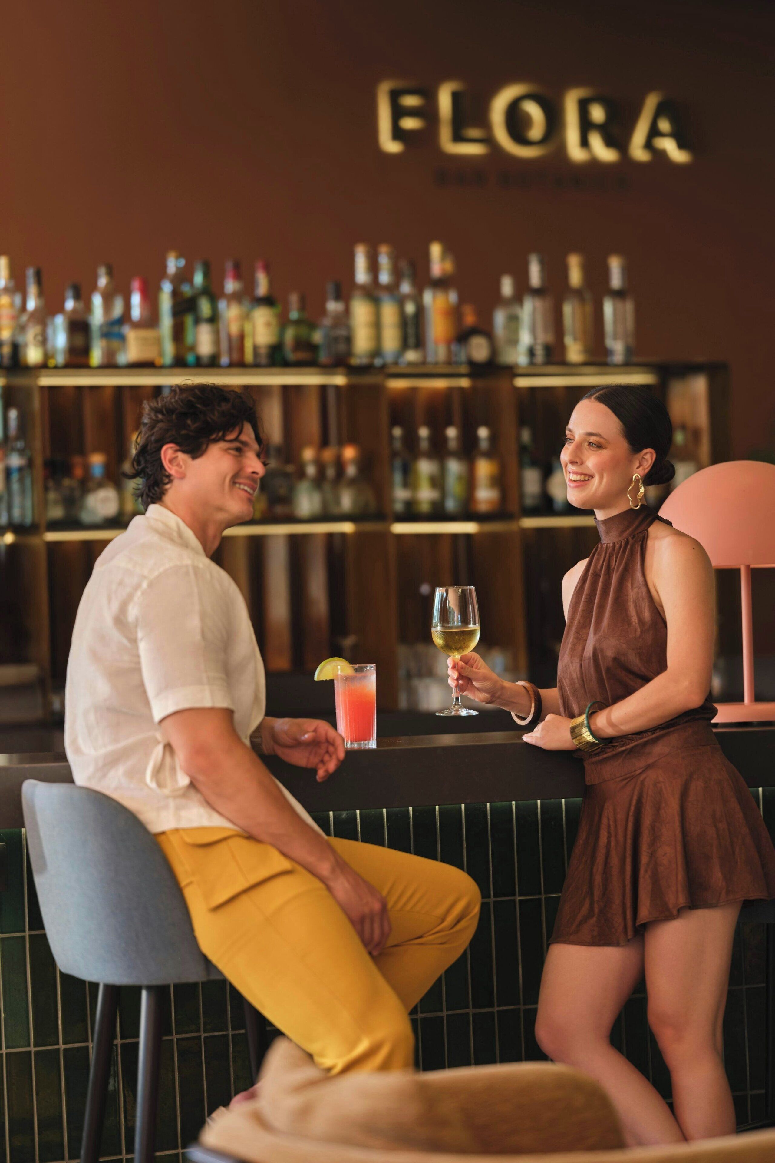 Un bar con una persona sentada y otra de pie, sosteniendo una bebida.