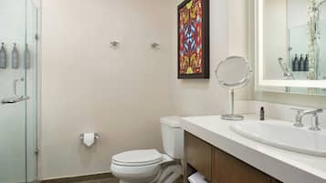A modern bathroom with a glass shower enclosure, a toilet, a sink with a mirror, and a framed artwork on the wall.
