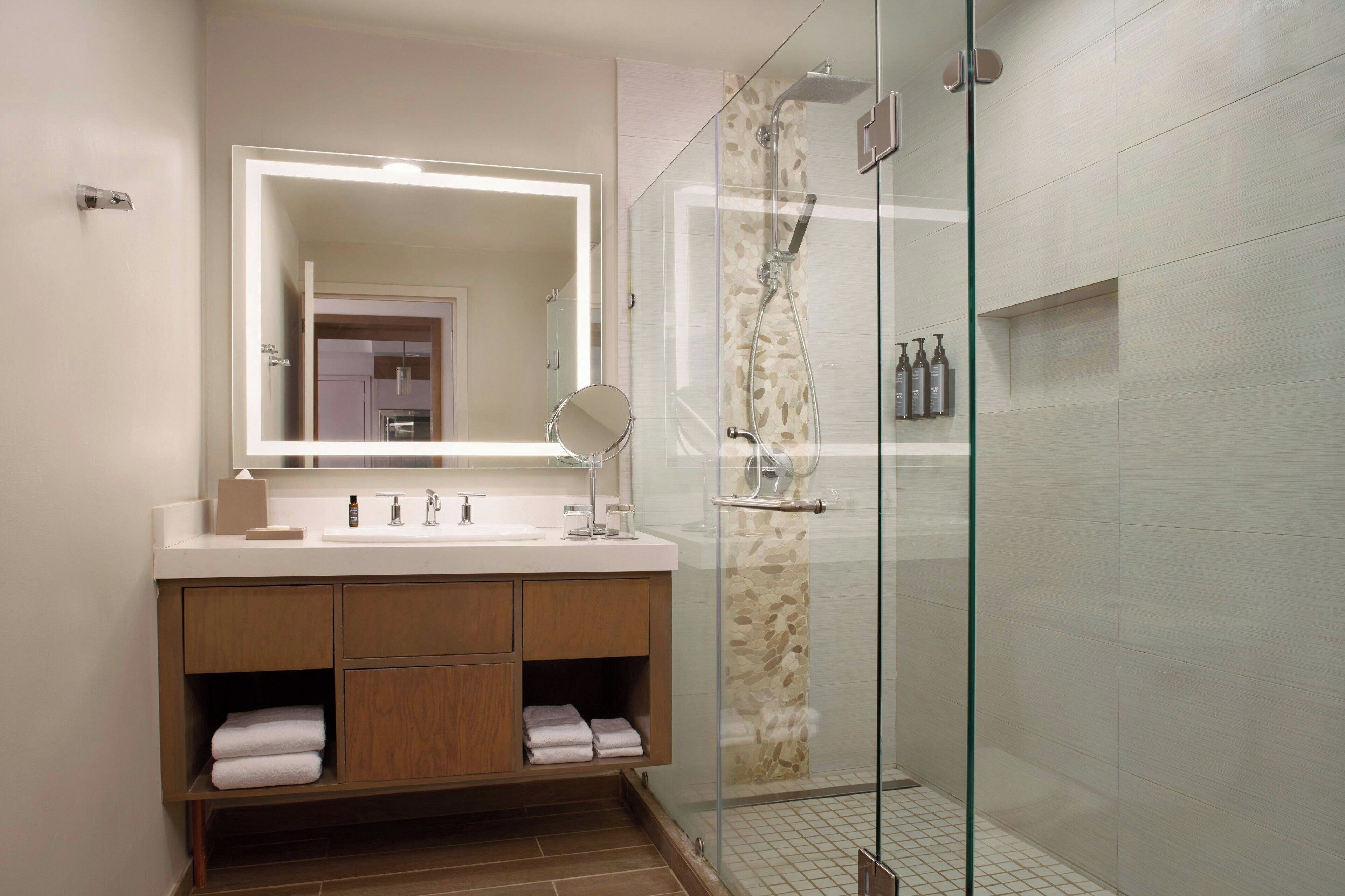 A modern bathroom with a glass-enclosed shower, a large mirror, and a wooden vanity.