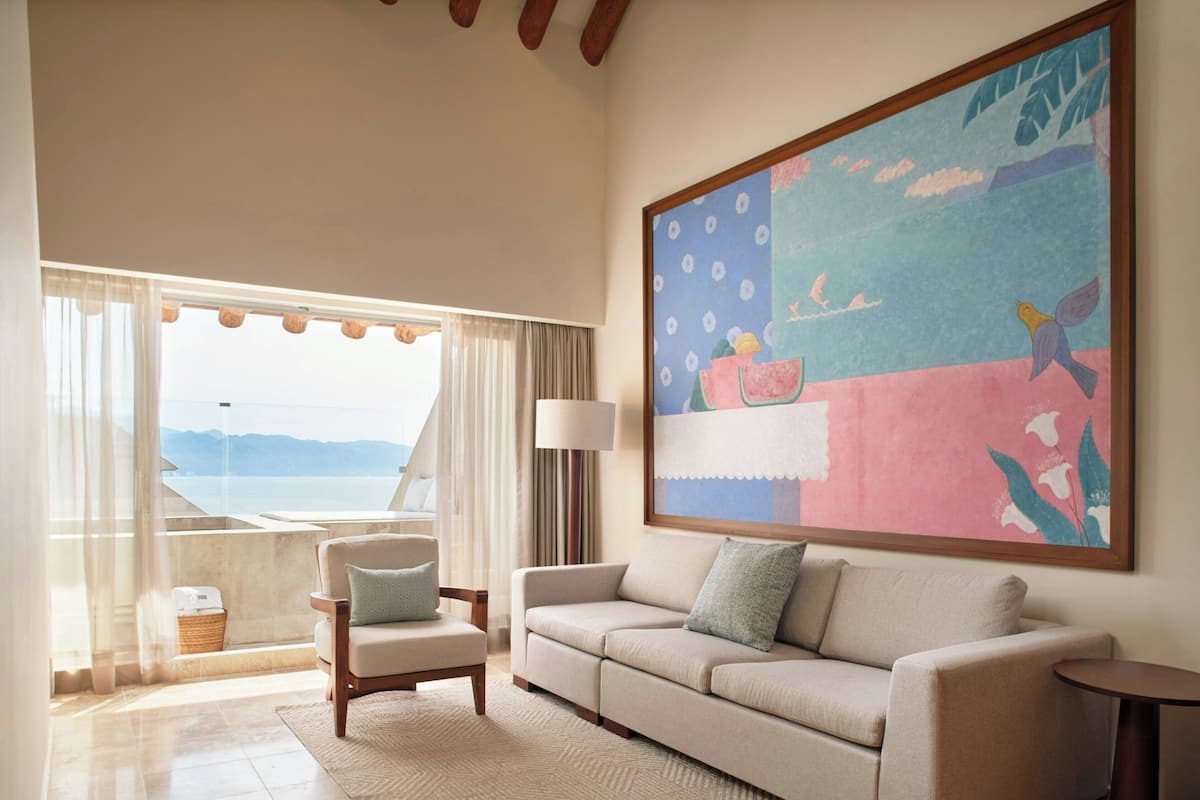 A living room with a sofa, armchair, and a large painting.