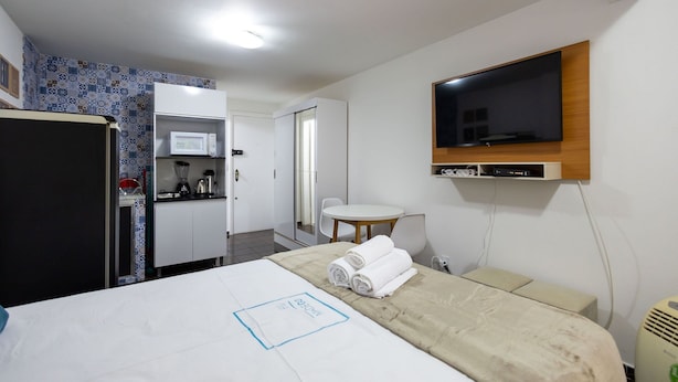 A hotel room with a bed, a TV mounted on the wall, a kitchenette, and a bathroom. - Beautiful Well-located Studio, Asa Norte Cbd112 (Brasília)