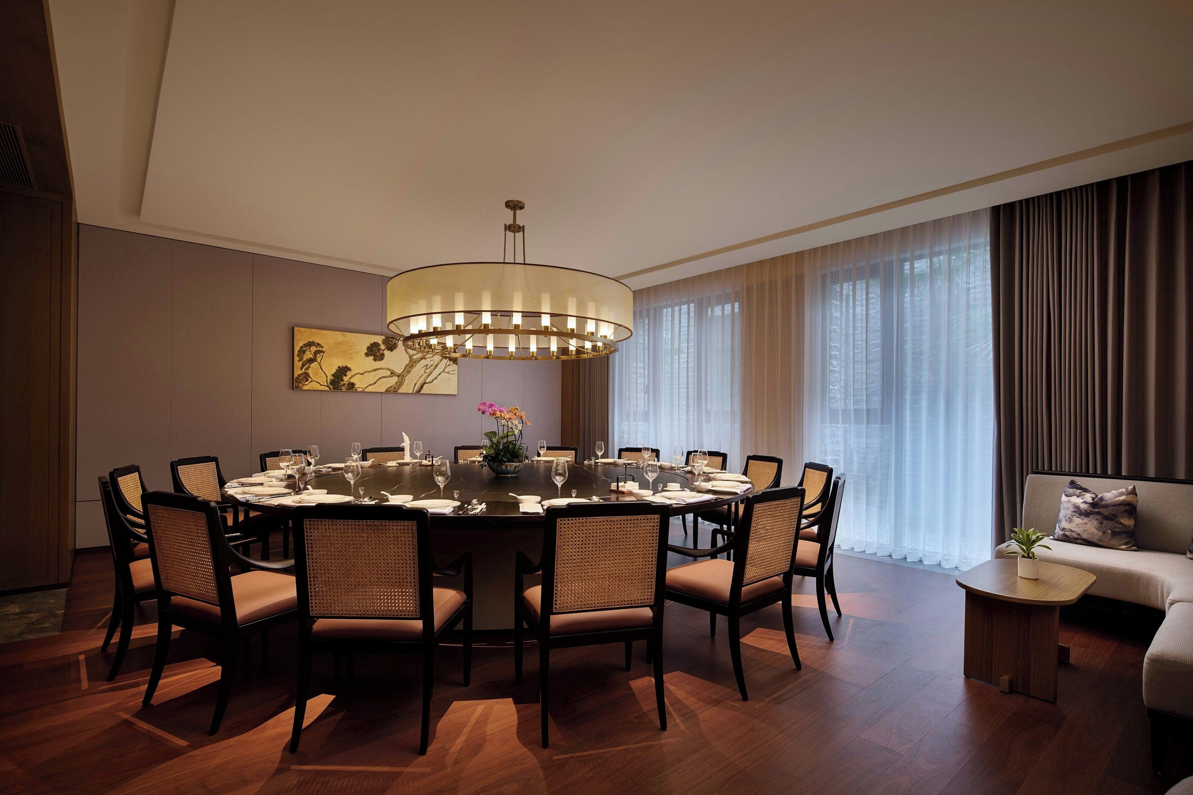 A modern dining room with a round table, six chairs, a chandelier, and a sofa.