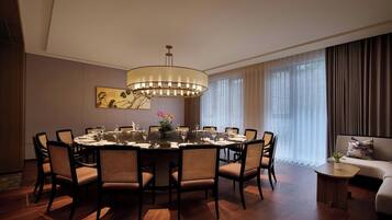 A modern dining room with a round table, six chairs, a chandelier, and a sofa.