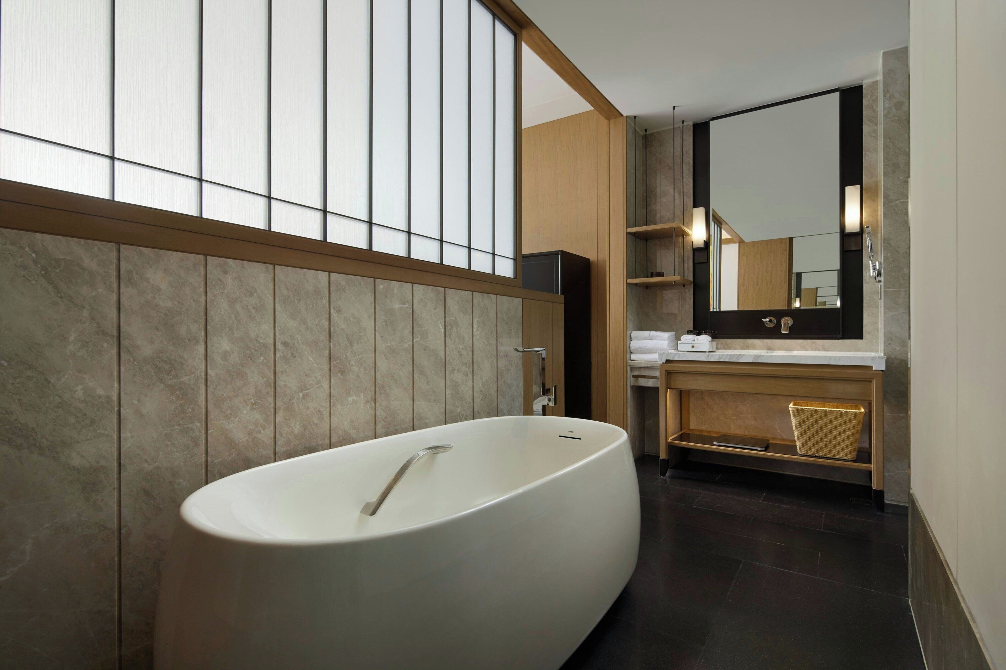 Een moderne badkamer met een vrijstaand bad, houten wandbekleding en een grote spiegel boven de wastafel.