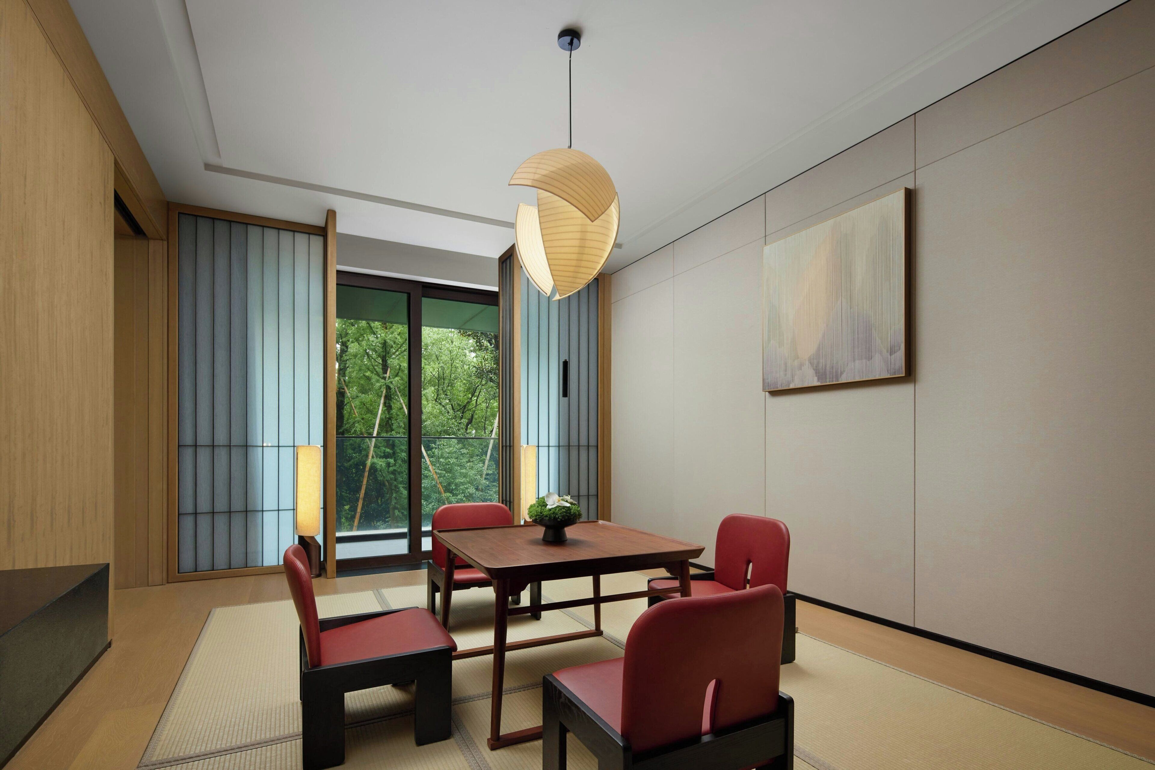 Un comedor moderno con una mesa de madera y sillas rojas, una lámpara colgante y vistas al exterior con vegetación.