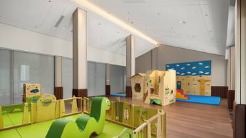 A spacious play area with soft play mats, wooden play structures, and a large window providing natural light.