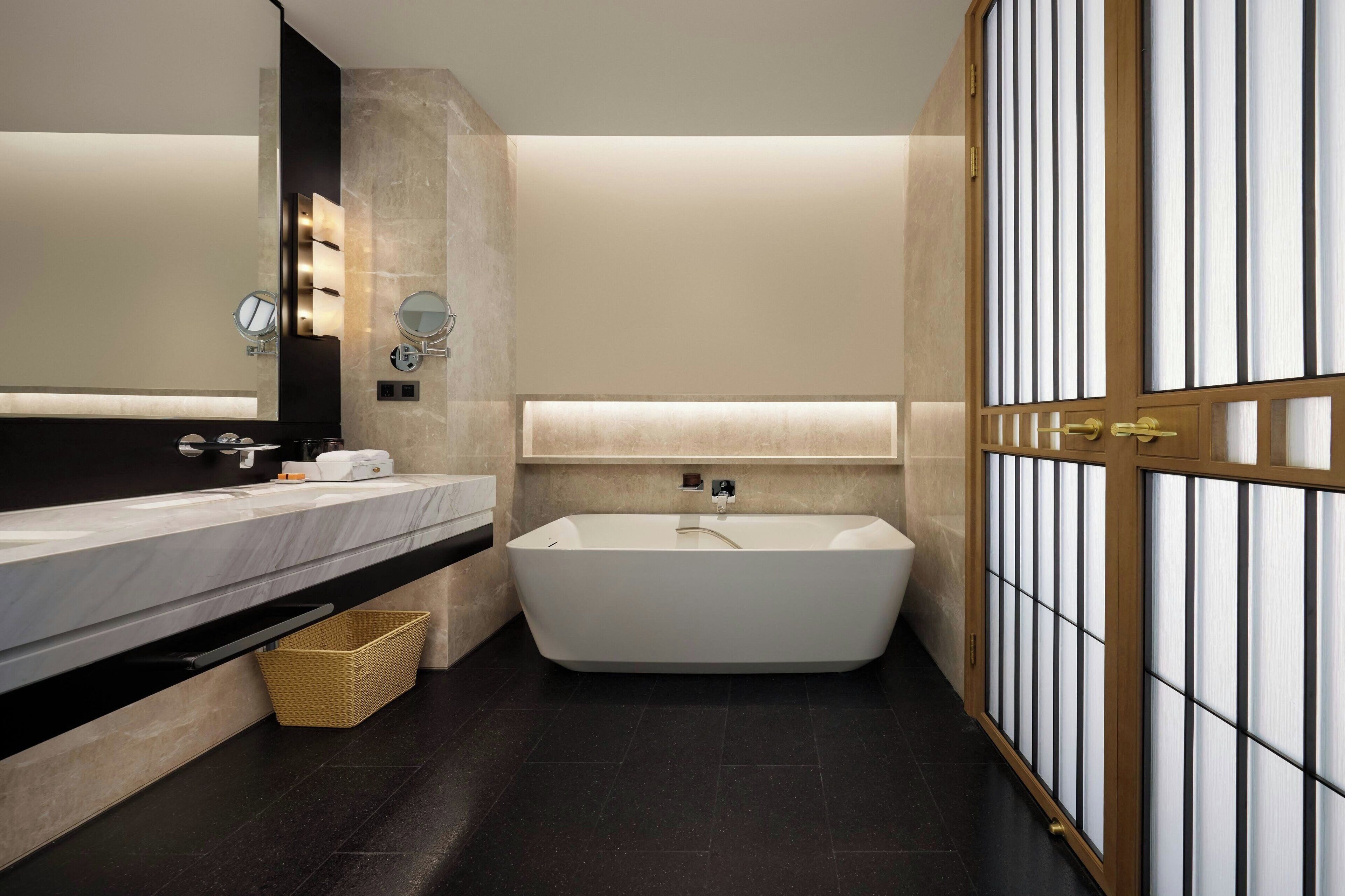 Un baño moderno con una bañera independiente, un espejo grande y un tocador con encimera de mármol.