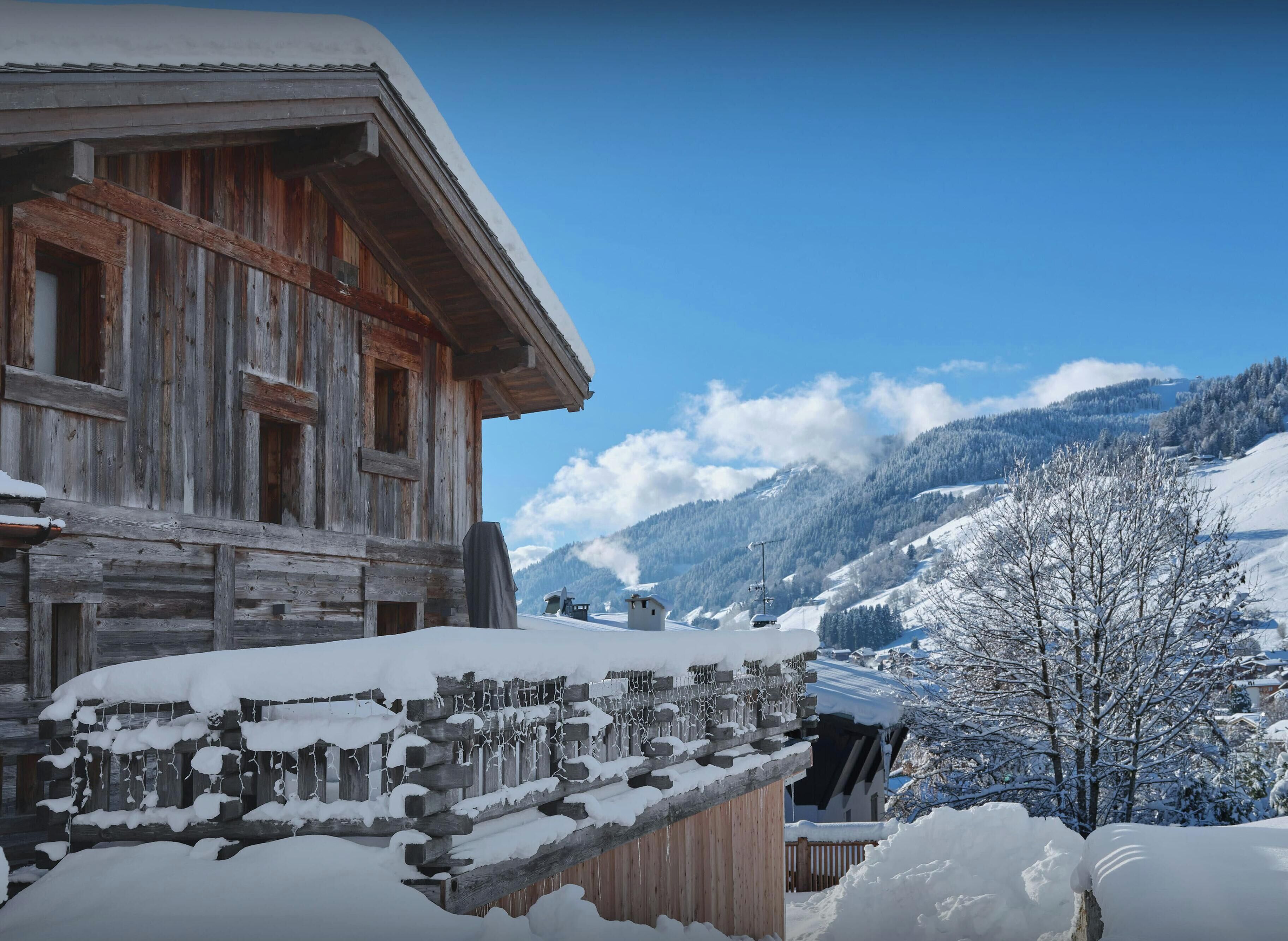 A wooden chalet with a snow-covered roof and a view of a mountainous landscape.