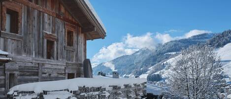 A wooden chalet with a snow-covered roof and a view of a mountainous landscape.