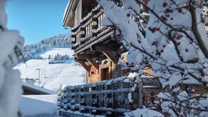 Una cabaña de madera con balcón cubierto de nieve y vistas a un paisaje montañoso nevado.