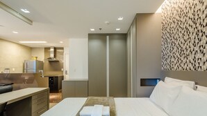 A hotel room with a bed, a desk, a kitchenette, and a bathroom.
